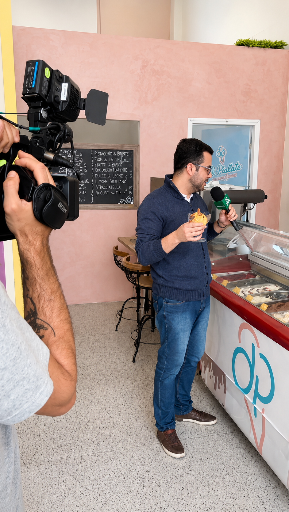 Gravação da reportagem com repórter da TV Evangelizar degustando taça de gelato em frente ao balcão Di Piallato